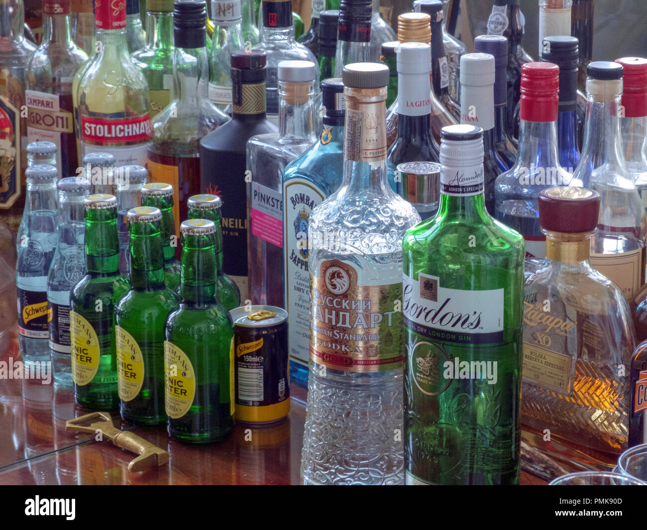 A side table full of many assorted bottles of spirits and mixers. Stock Photo
