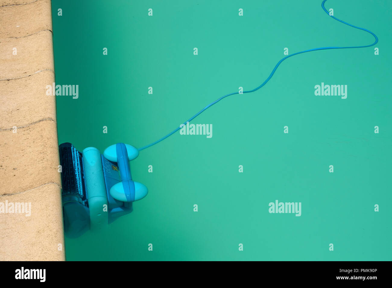 An automatic robot pool cleaner climbs the side of a cloudy swimming