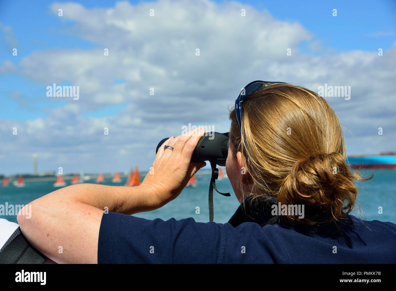 Rear view of woman with binoculars on sunny day watching yacht racing during Lendy Cowes Week (2018), Isle of Wight, UK Stock Photo