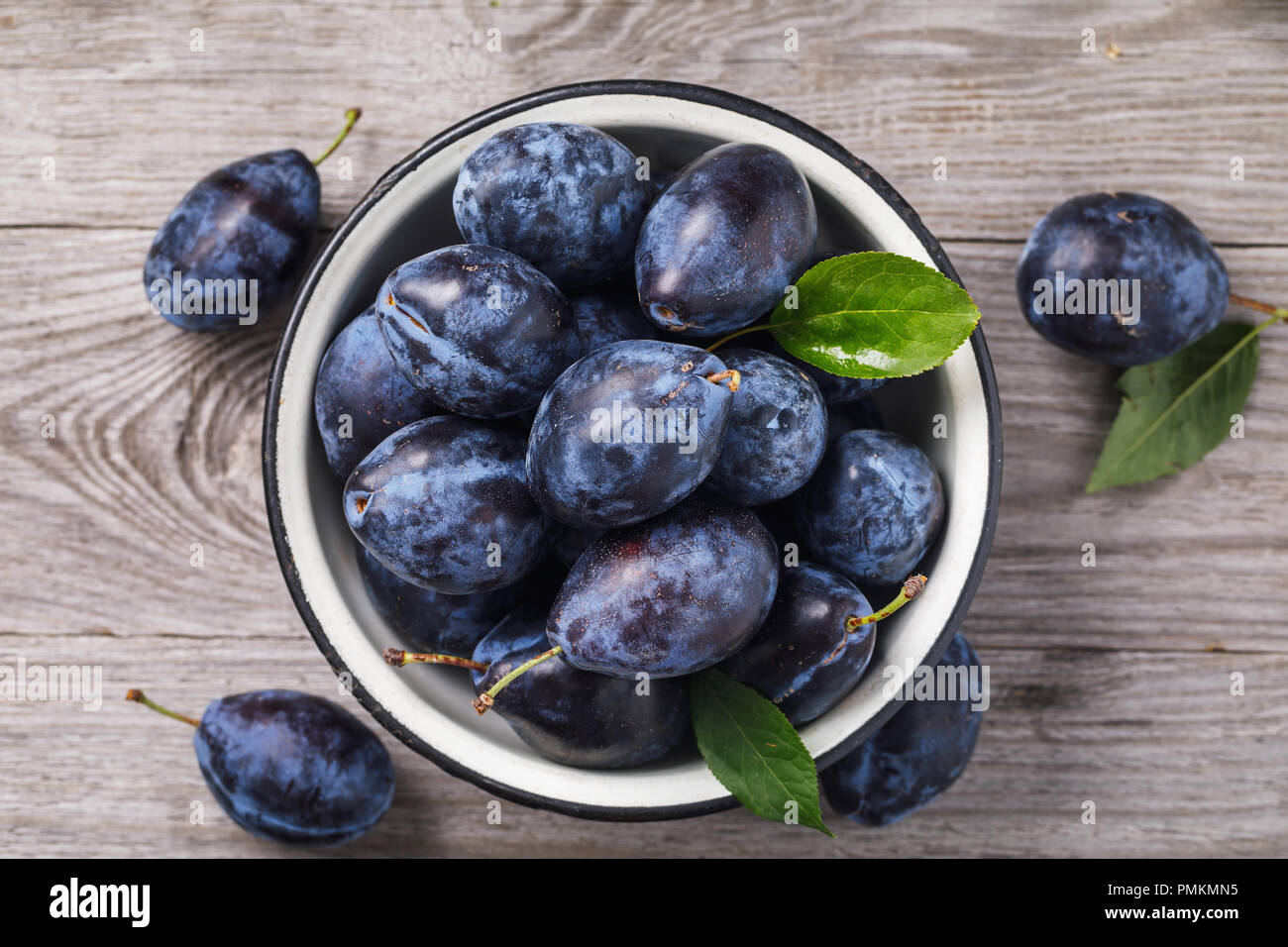 Metal bowl full of ripe prune fruit on a wooden table, top view Stock Photo
