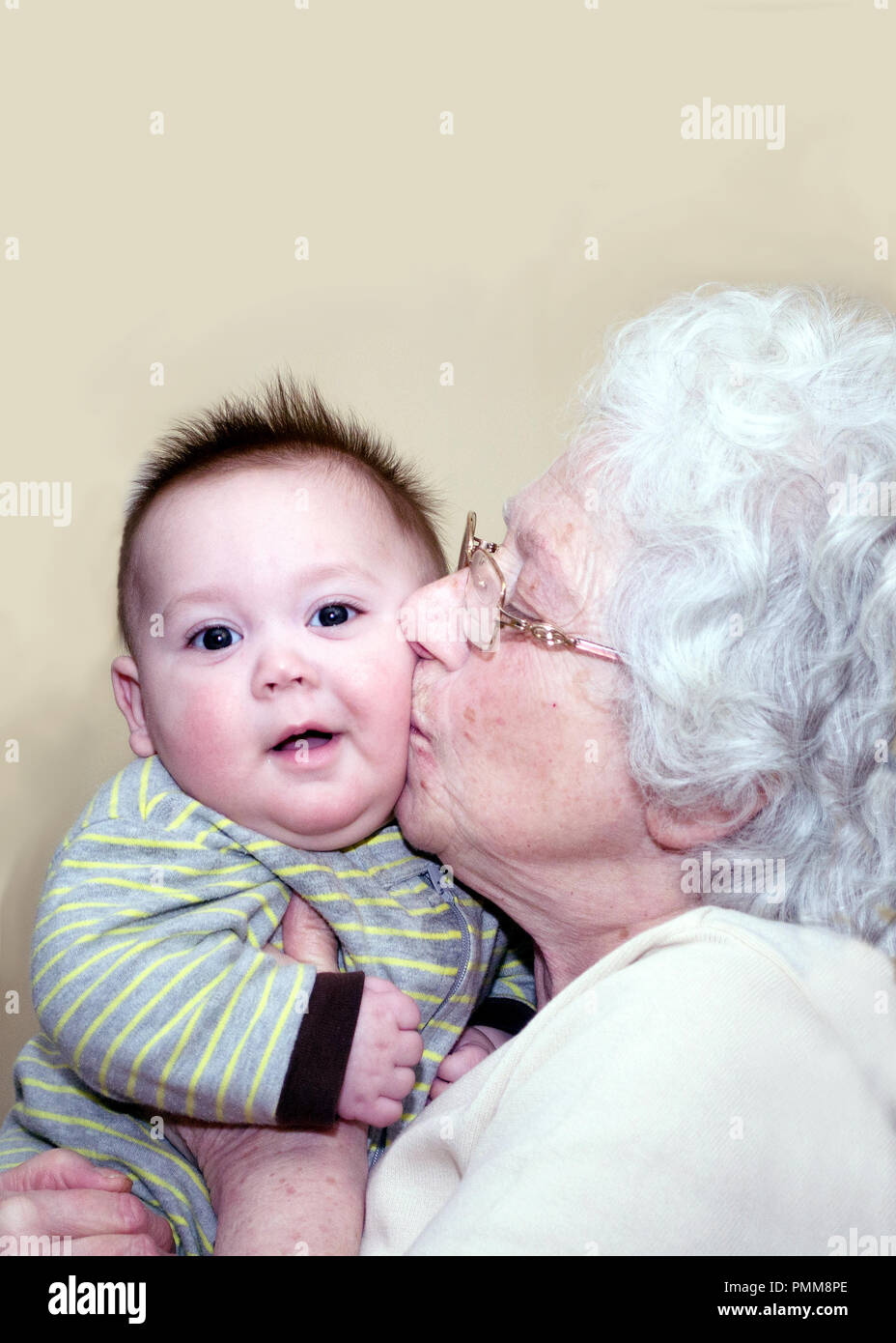 Grandma kissing chubby cheeks of a baby who is smiling with happiness Stock Photo