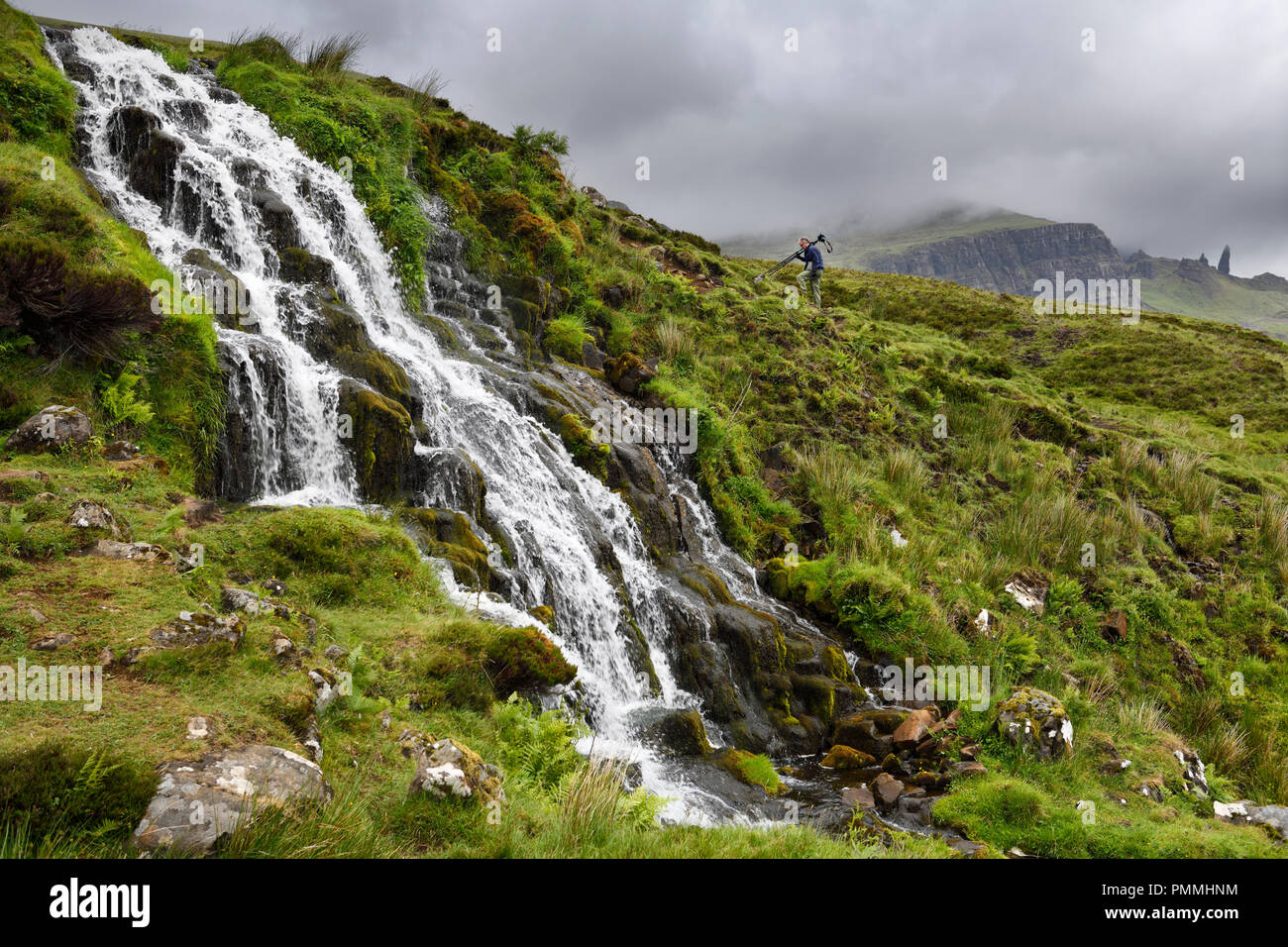 Photographer hiking up Brides Veil WaterFalls at The Storr with Old Man of Storr peak in clouds on Isle of Skye Inner Hebrides Scotland UK Stock Photo