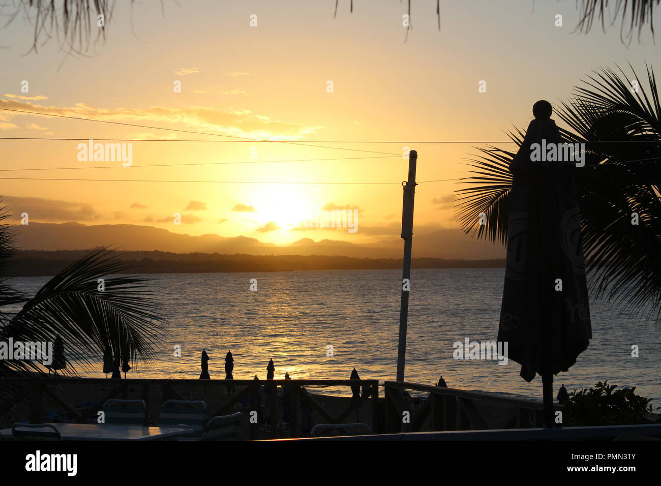 Sunset across the bay in Sosua, Dominican Republic with beach umbrella and palm trees in silhouette Stock Photo