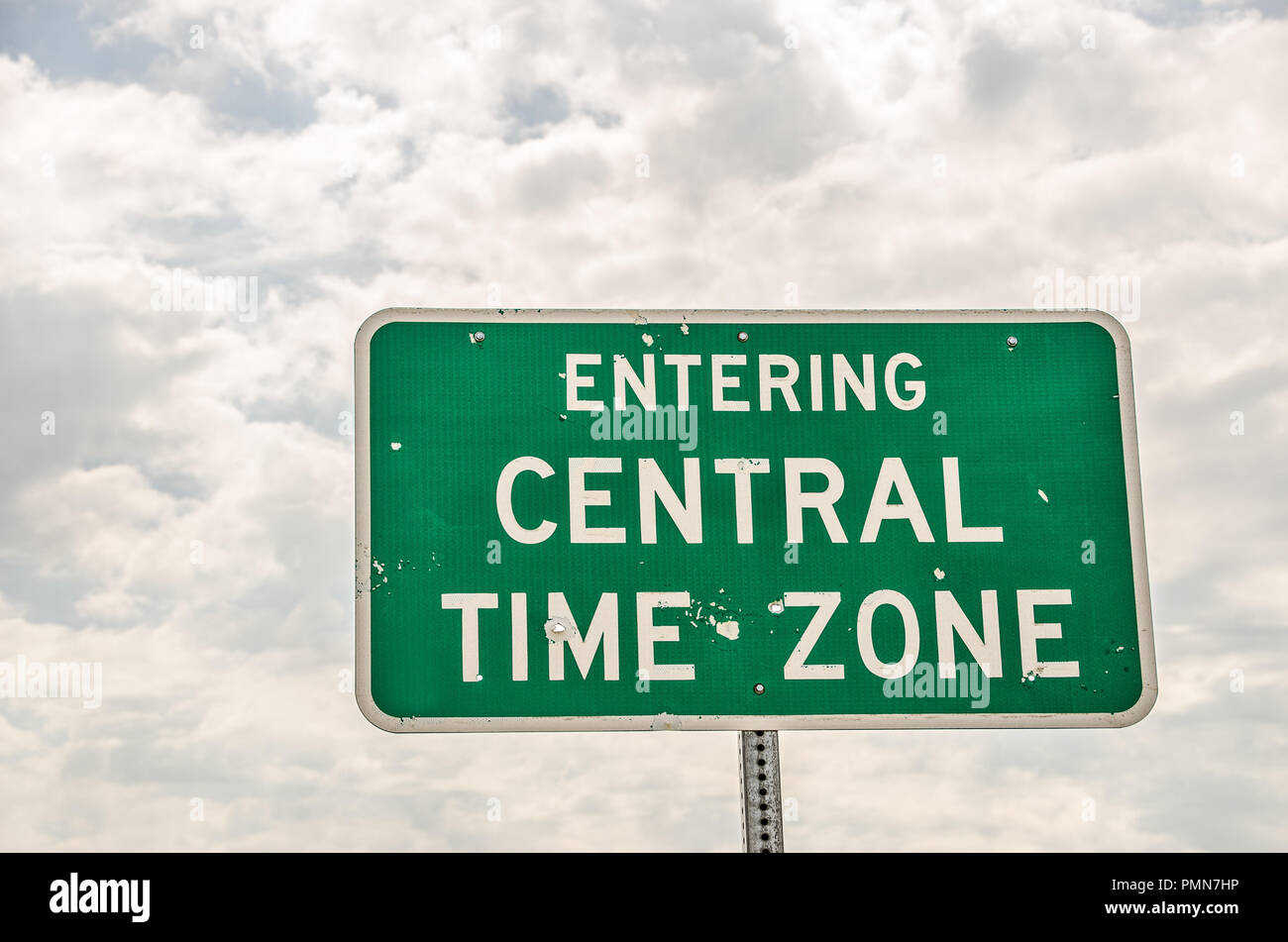 Green and white sign with bullet holes letting travelers know they are entering the central time zone Stock Photo