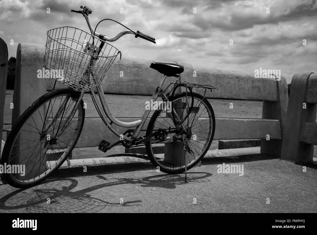 Vintage lonely bicycle parked on concrete road by the river with grey sky and clouds. Travel alone. Lonely life.  Worthless or abandoned bike. Hopeles Stock Photo