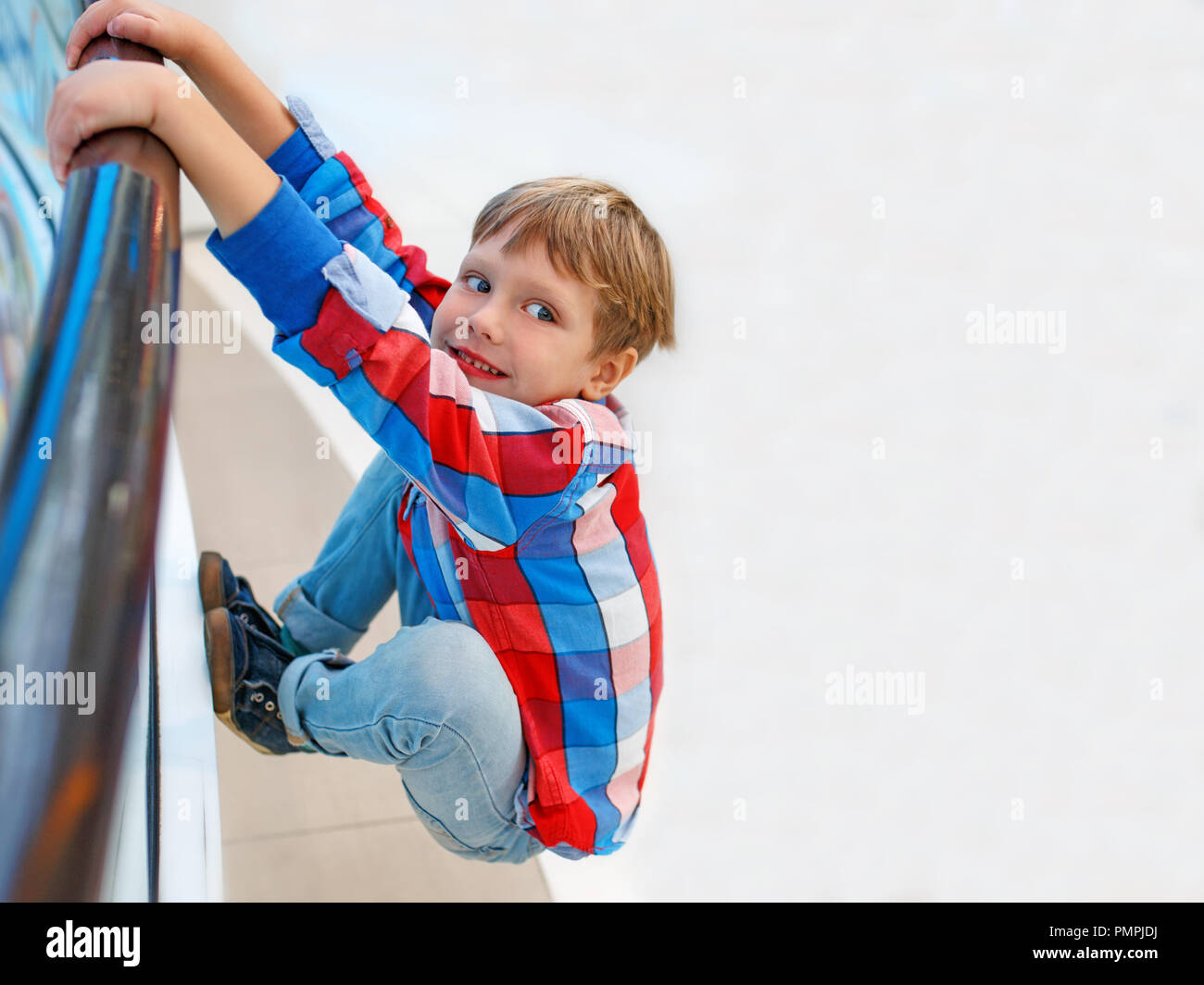 Boy is hanging on the railing of the bridge, child playing in a park Stock Photo