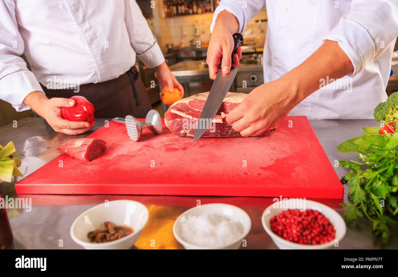 Cooking process concept. Portrait of two working men in cook uniform making food in modern kitchen. Indoor shot. Stock Photo