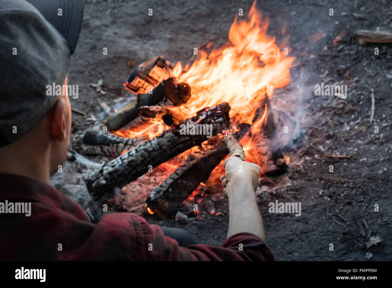Making campfire at a forest. Male person in casual clothes puts pieces