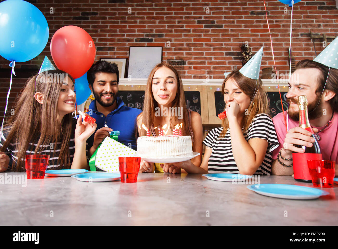 Gorgeous young brunette woman celebrating her birthday getting ready to blow out the candles on the cake watched by a smiling group of friends Stock Photo