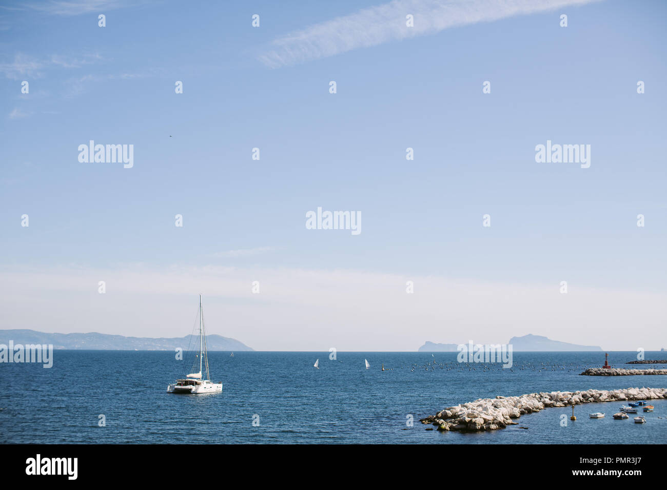 One catamaran sailing out of harbour on calm blue sea on a summer's day in the Mediterranean Stock Photo