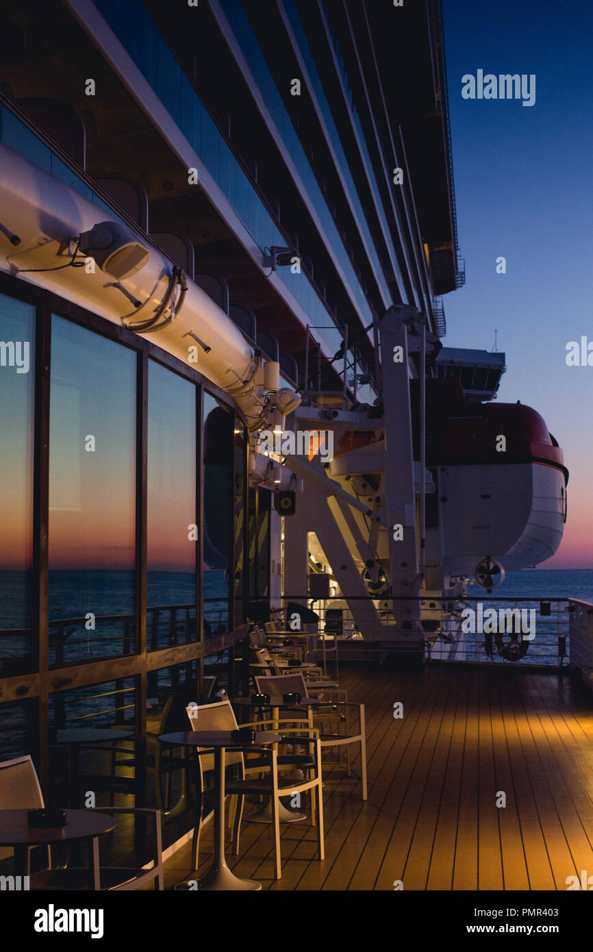 Evening shot of the exterior (promenade deck) of a cruise ship with the sea in the background and a glowing sunset reflected in the windows Stock Photo