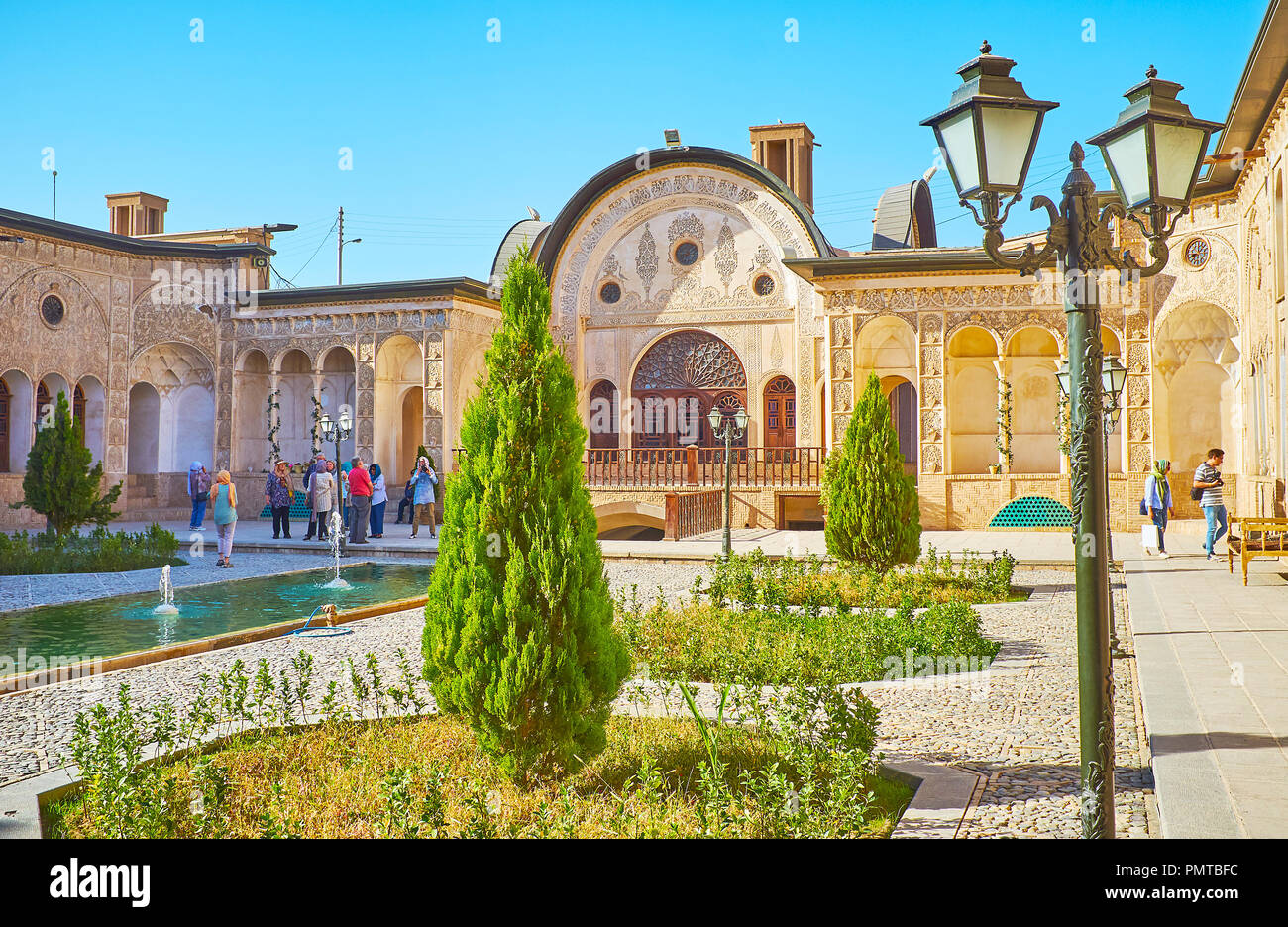 KASHAN, IRAN - OCTOBER 22, 2017: The small garden of Tabatabaei House with young thuja trees, octagonal flower beds, fountains and the vintage streetl Stock Photo