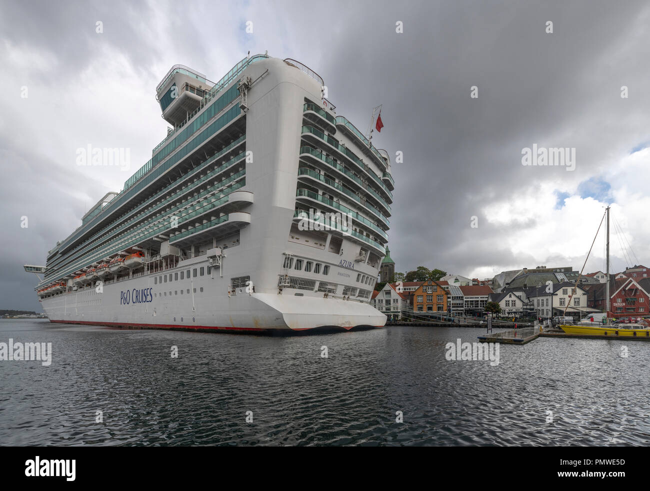 The gigantic P&O cruise ship Azura in the tiny port of Stavanger in Norway. Vastly out-sizing the local buildings. Exciting and horrific in scale. Stock Photo