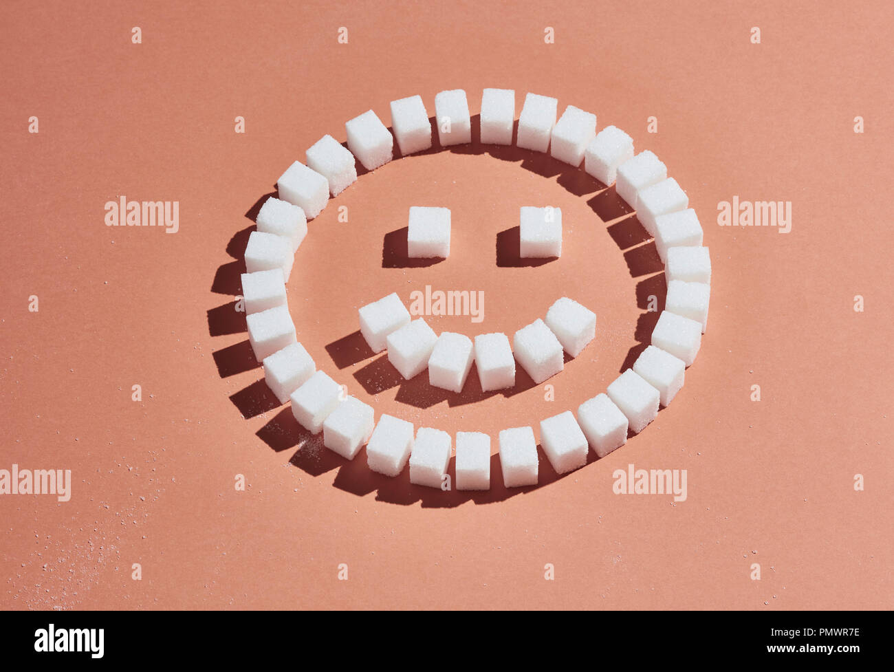 Sugar cubes forming smiley face on peach background Stock Photo