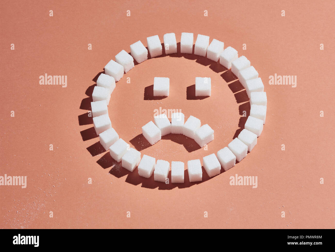 Sugar cubes forming frowning face on peach background Stock Photo