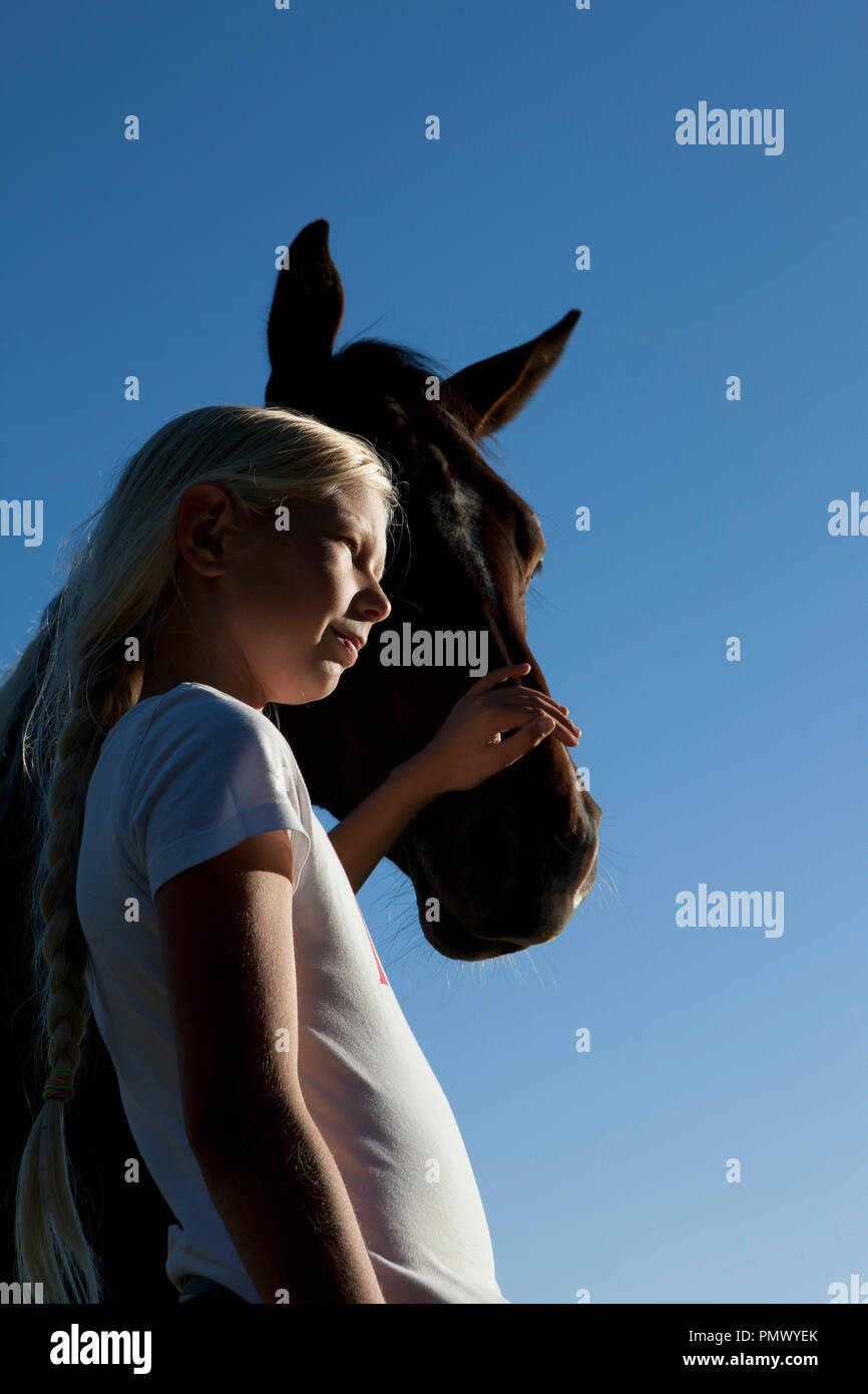 Girl petting horse muzzle under blue sky Stock Photo