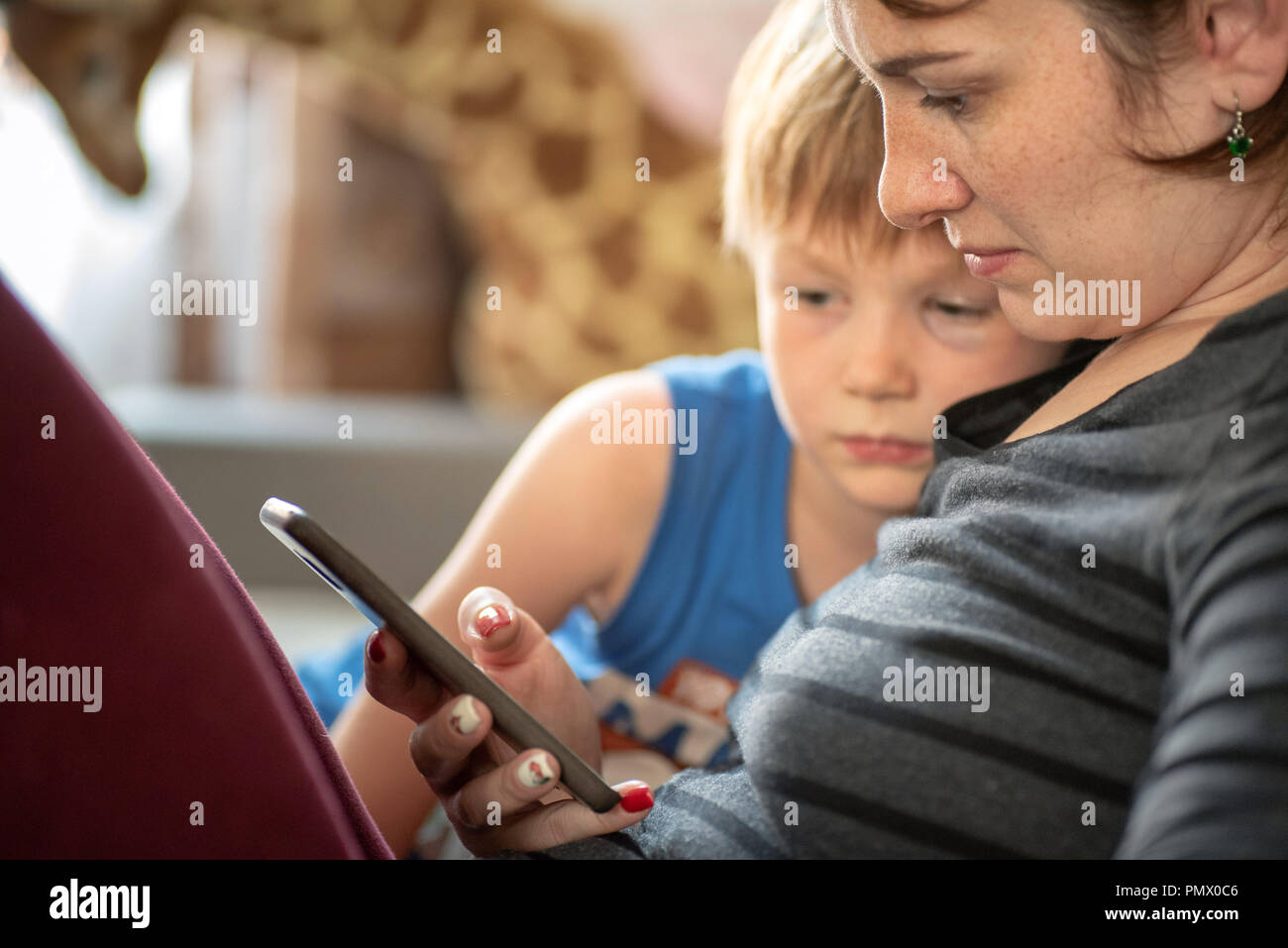 Mother and son using smartphone tablet on sofe at home. Stock Photo