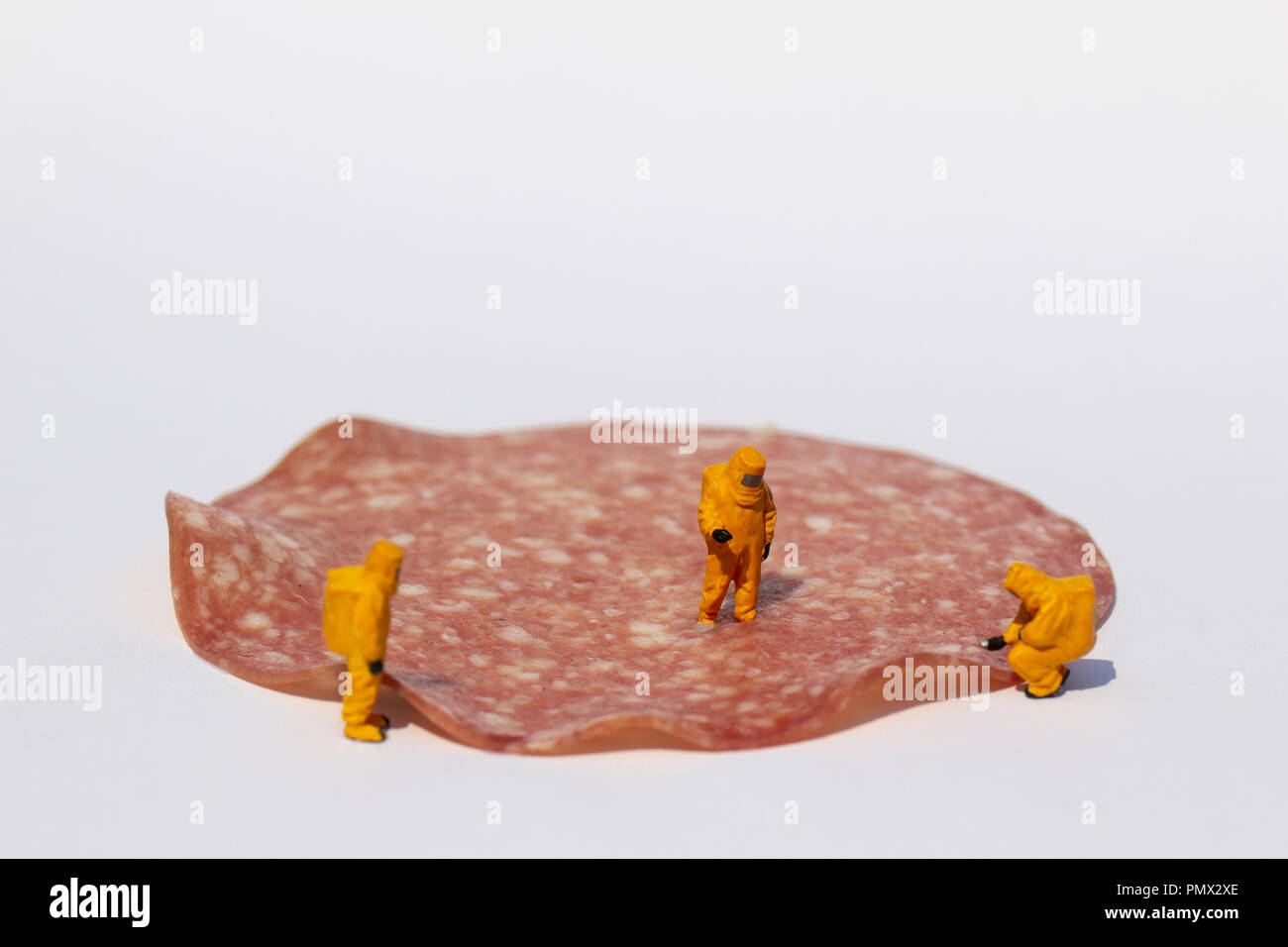 Small scientists in clean suits examining salami for bacteria Stock Photo
