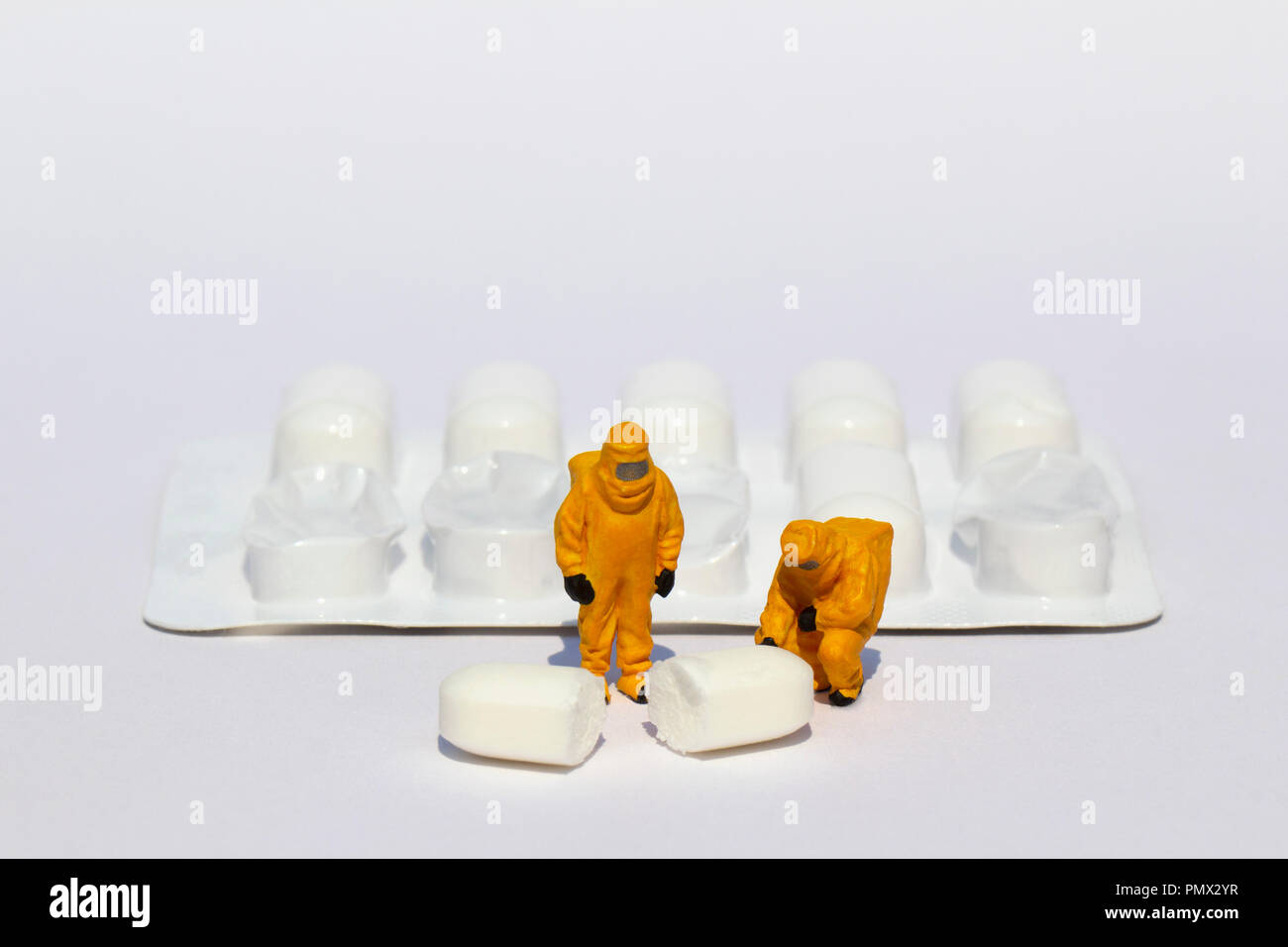 Small scientists in clean suits examining white tablet from blister pack Stock Photo