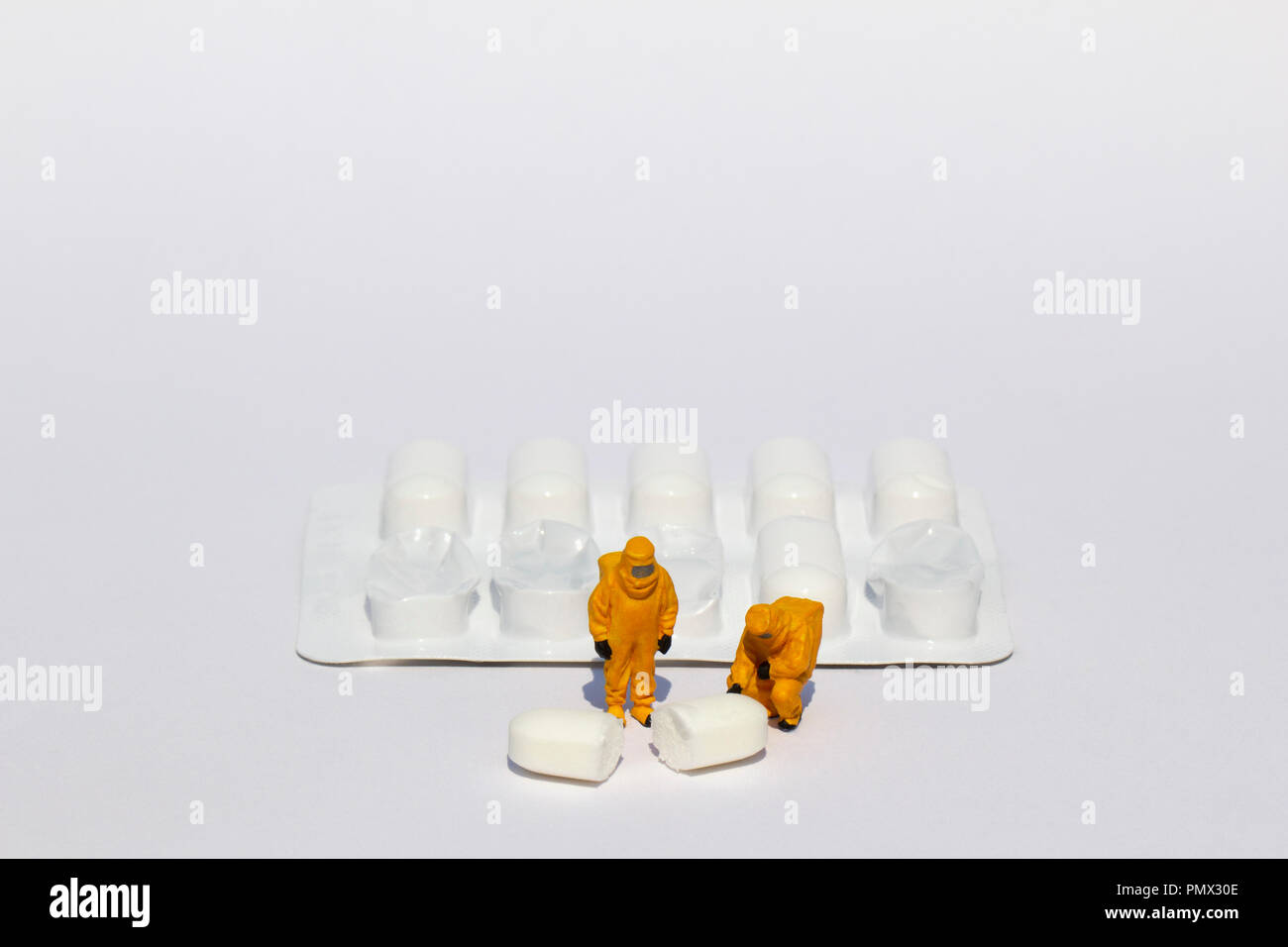 Small scientists in clean suits examining white tablet from blister pack Stock Photo