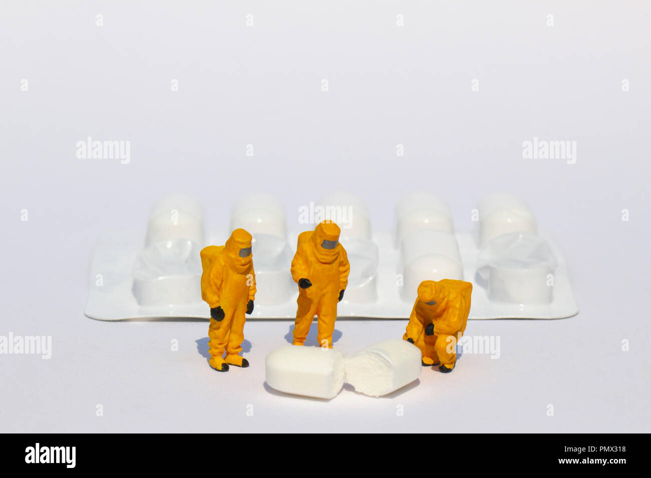Small scientists in clean suits examining white tablet from blister pack Stock Photo