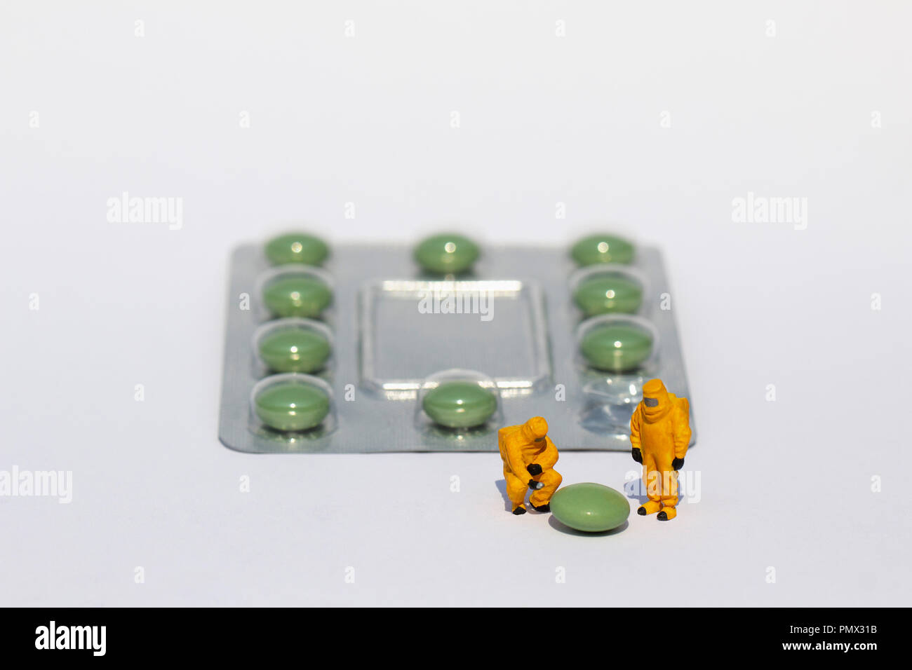 Small scientists in clean suits examining green pill from blister pack Stock Photo
