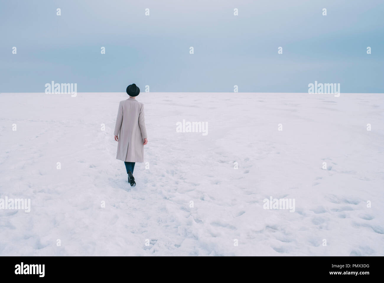 Woman in coat and hat walking in snow covered landscape Stock Photo
