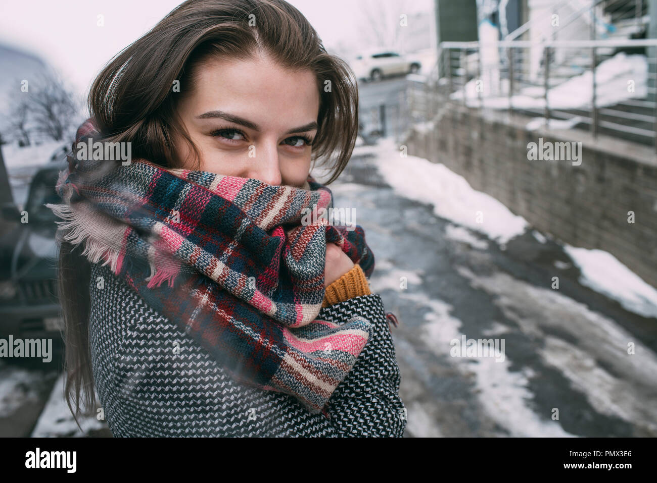 Portrait confident young woman in plaid scarf on snowy winter street Stock Photo