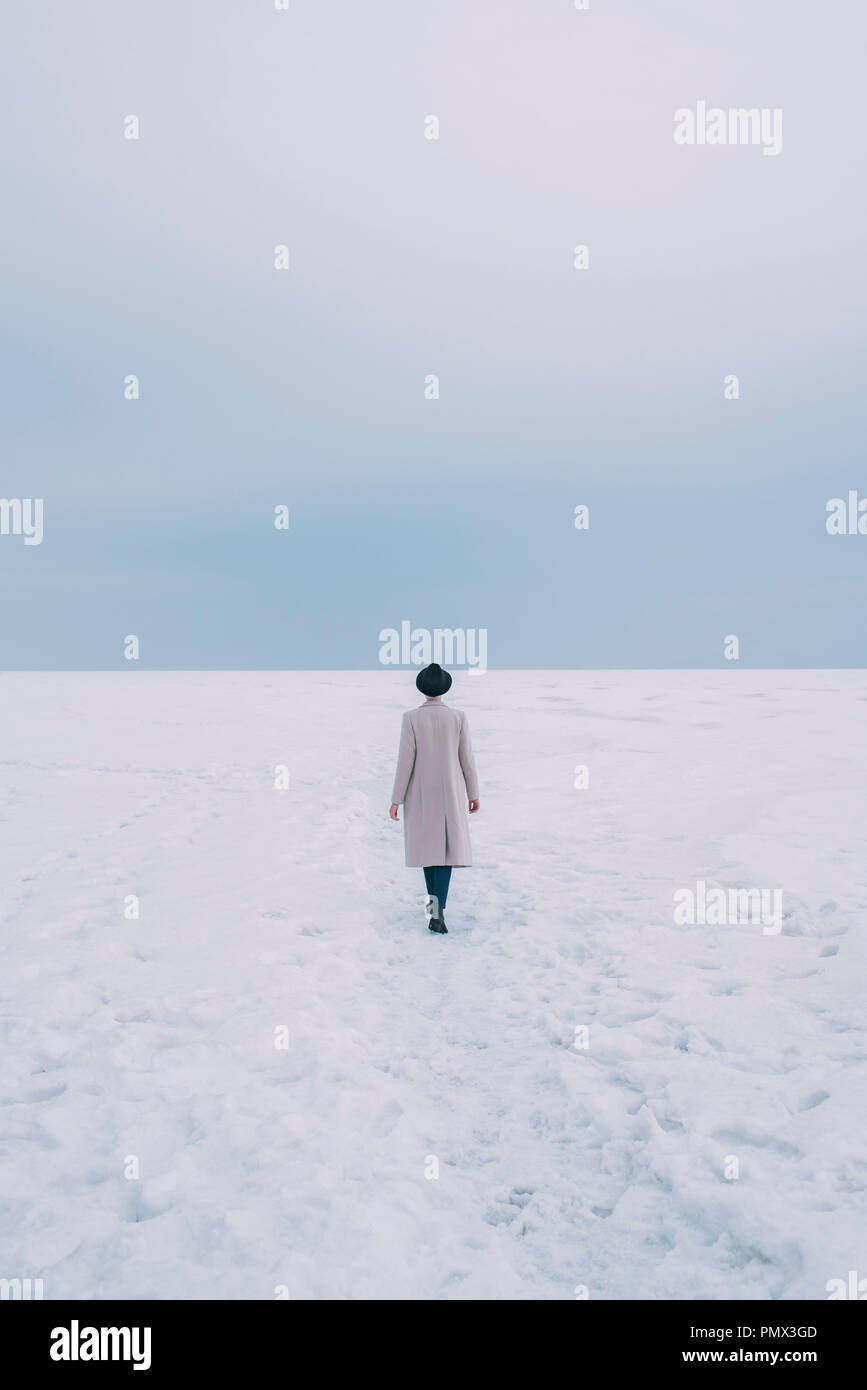 Woman in coat and hat walking in snow covered landscape Stock Photo