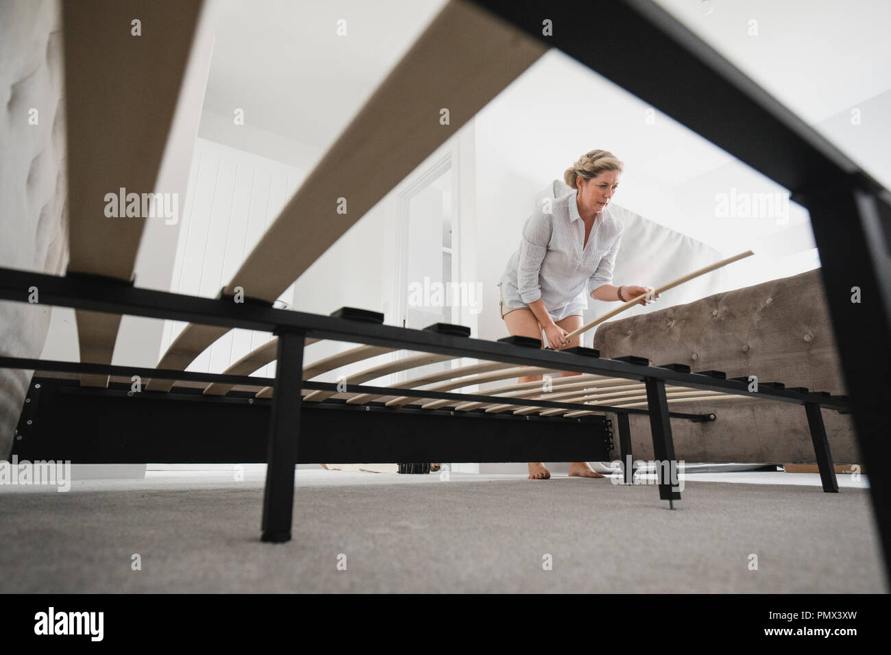 Low angle view of a mature woman setting up her bed in her new home. Stock Photo