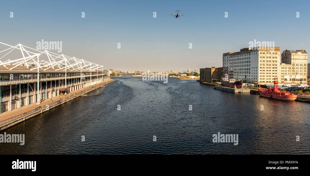 London, England, UK - September 2, 2018: A small passenger airplane flys low over Royal Victoria Dock, flanked by the ExCeL exhibition centre and Mill Stock Photo