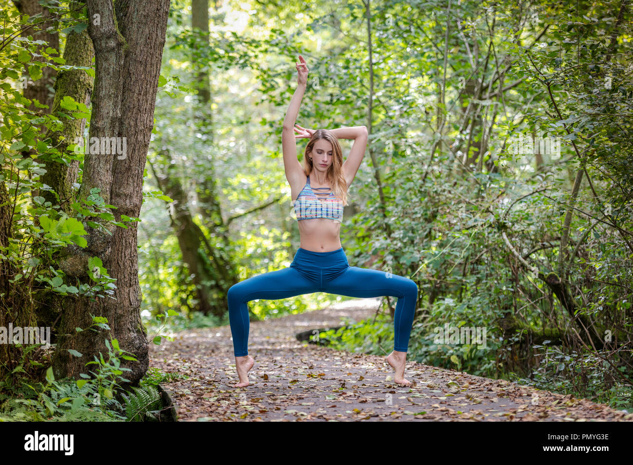 young woman practicing yoga in the woods on a wooden boardwalk Stock