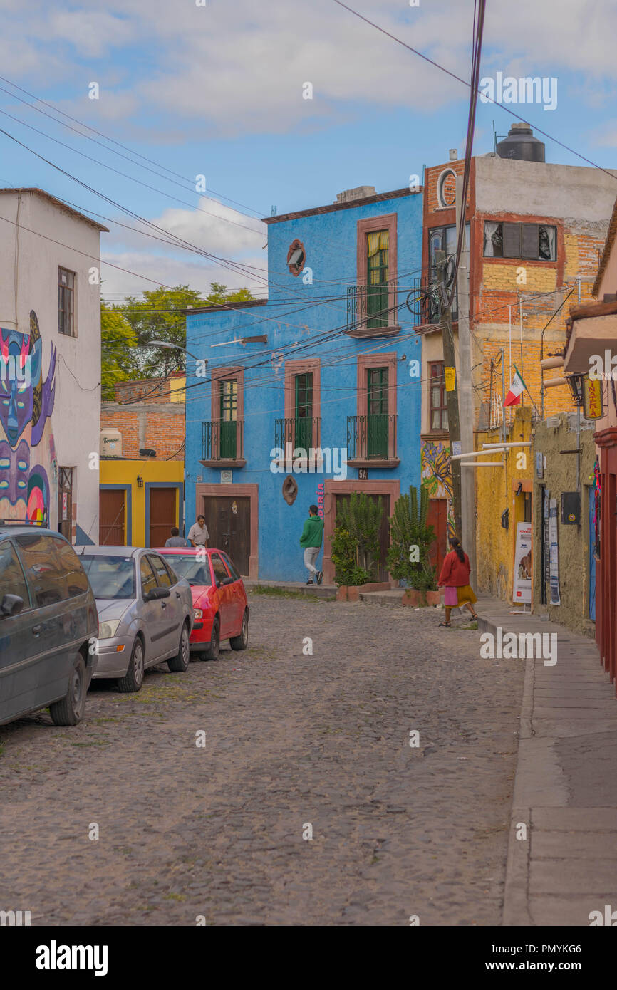 Charming cobblestone street, with some cars, pedestrians and a big blue house, in San Miguel de Allende, Mexico Stock Photo