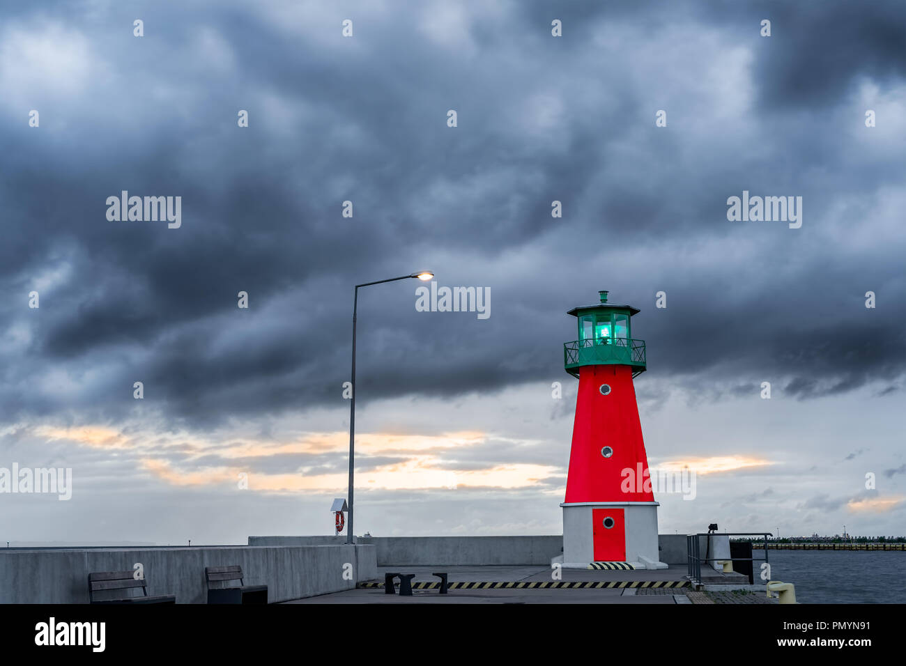 Red and green lighthouse on a harbor pier against dramatic clouds in the sky. Stock Photo