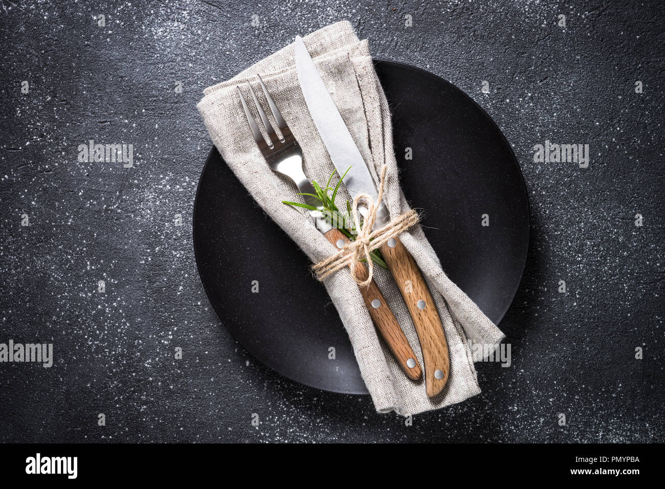 Black plate, cutlery and napkin on stone table top view. Stock Photo