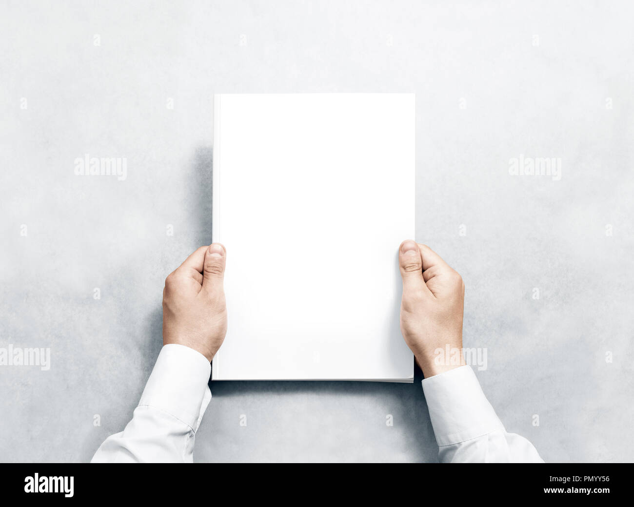 Hand holding white journal with blank cover mockup. Arm in shirt hold clear magazine template mock up. A4 book softcover surface design. Paperback pri Stock Photo