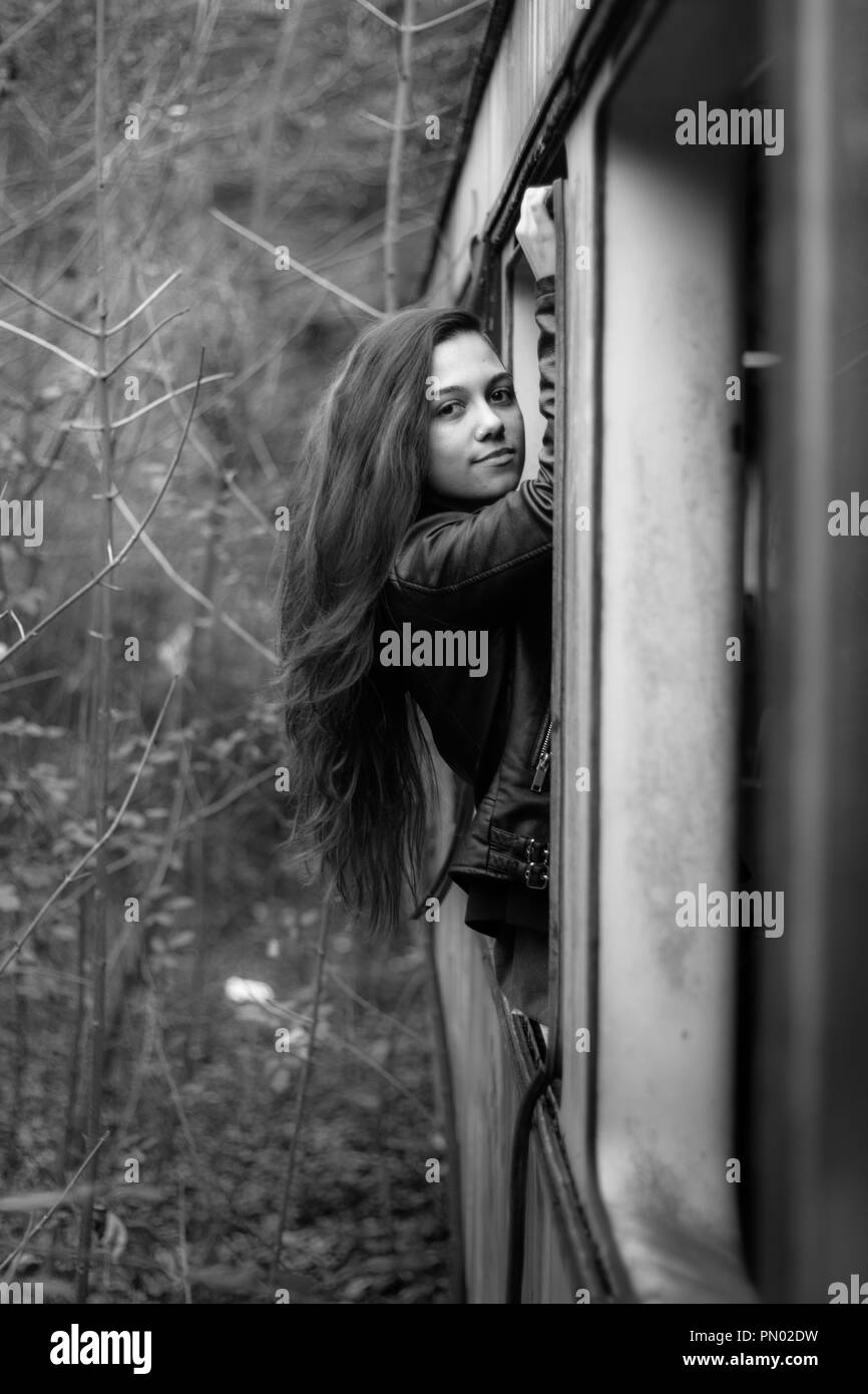 Young brunette woman hanging out of an abandoned train window in the woods with long red hair Stock Photo