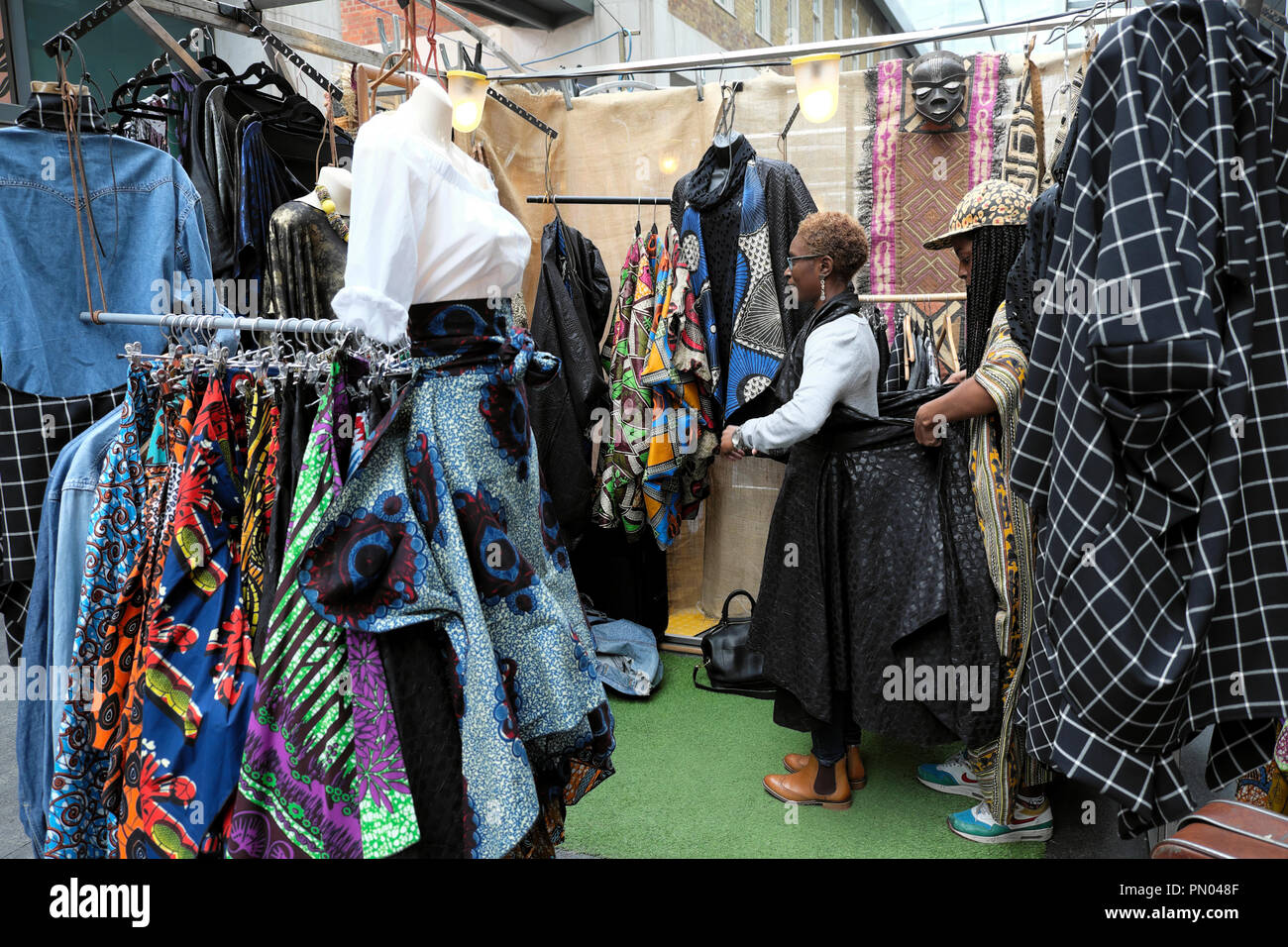 A woman trying on dress in clothing shop selling African textiles fabric clothing in Spitalfields Market in East London UK,  KATHY DEWITT Stock Photo