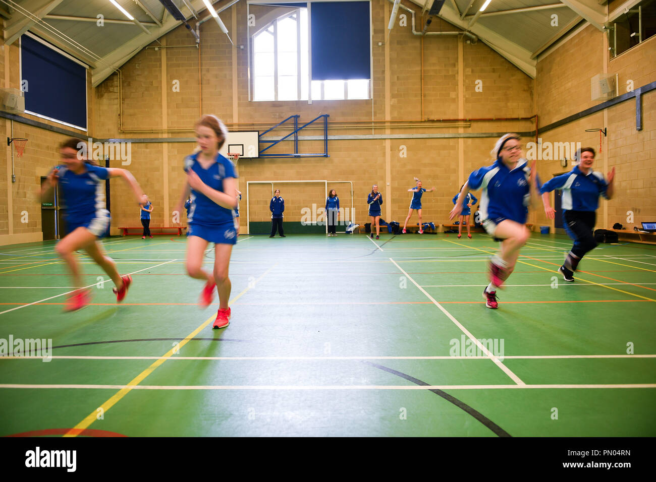 Students run during a Physical Education (PE) lesson inside the gymnasium sports hall at Royal High School Bath, which is a day and boarding school for girls aged 3-18 and also part of The Girls' Day School Trust, the leading network of independent girls' schools in the UK. Stock Photo