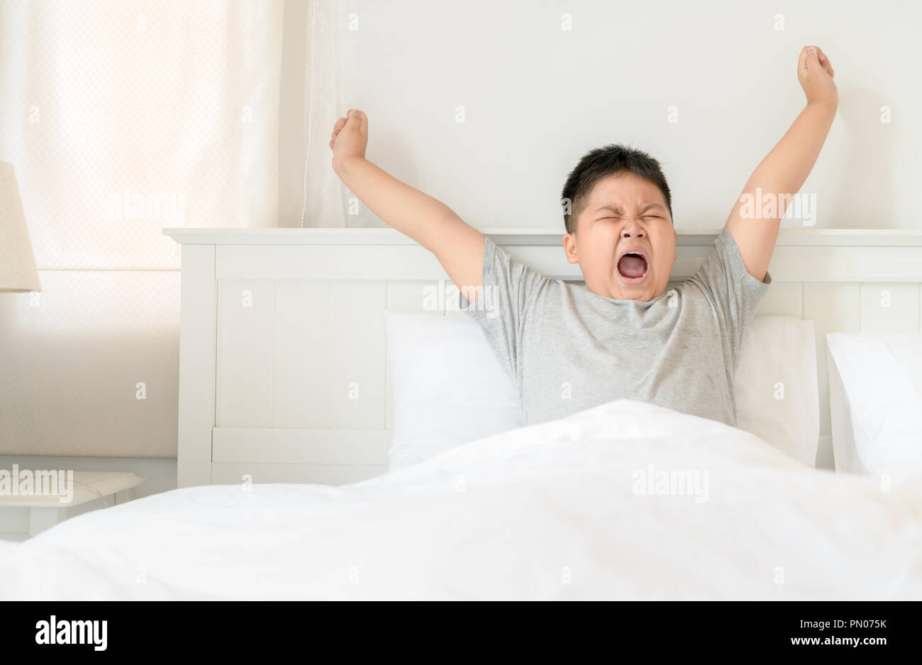 Obese boy wake up yawning and stretch on bed in morning. lazy concept Stock Photo