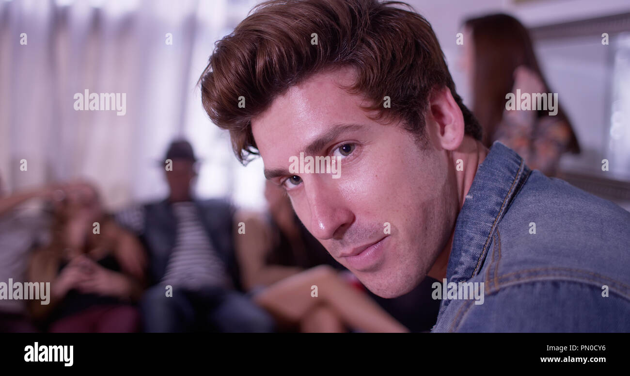 Portrait of Handsome young hipster man smiling at camera with group of friends partying in background Stock Photo