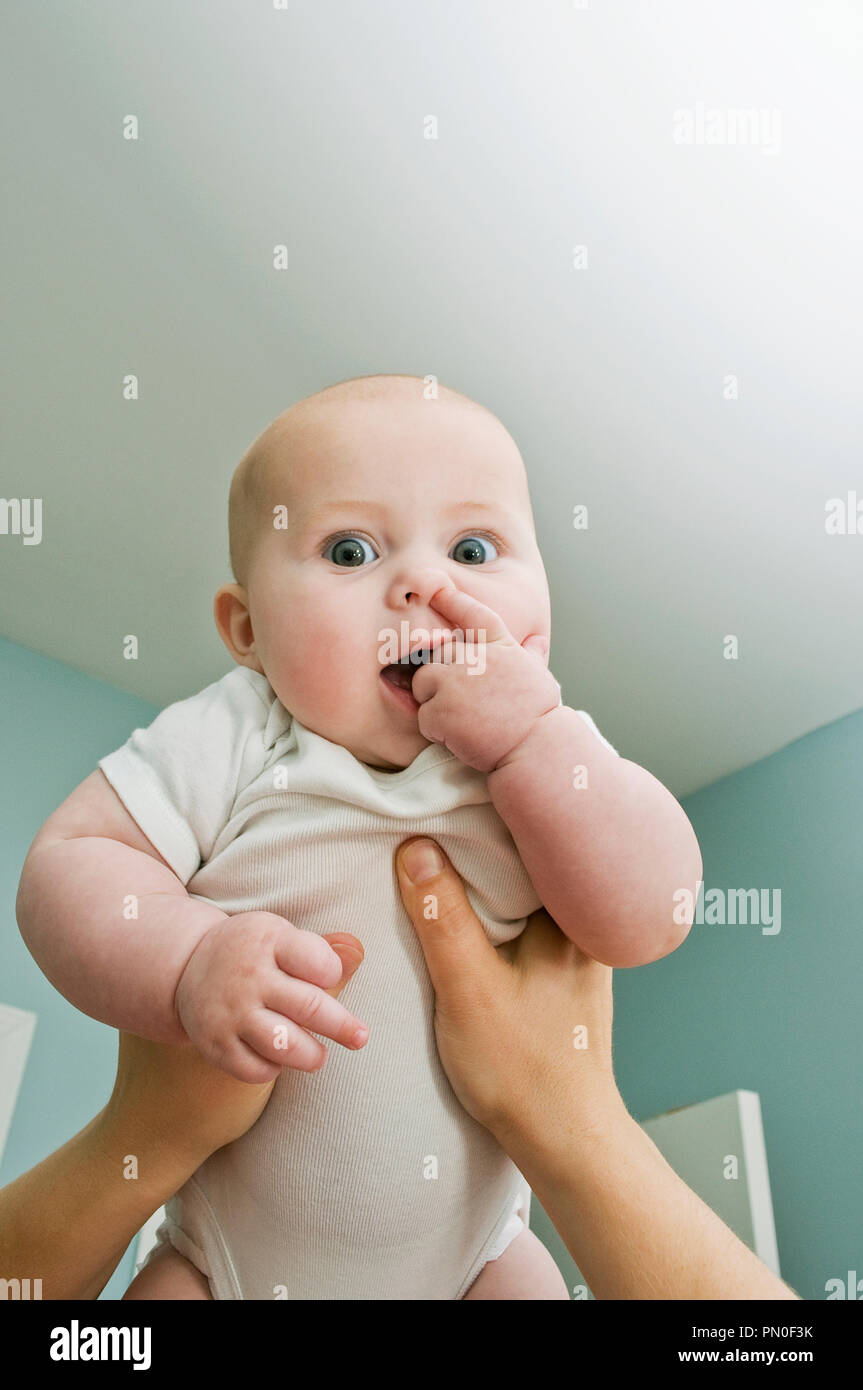 A woman holding up her 6 month old baby girl, (six months) picking her nose. Stock Photo