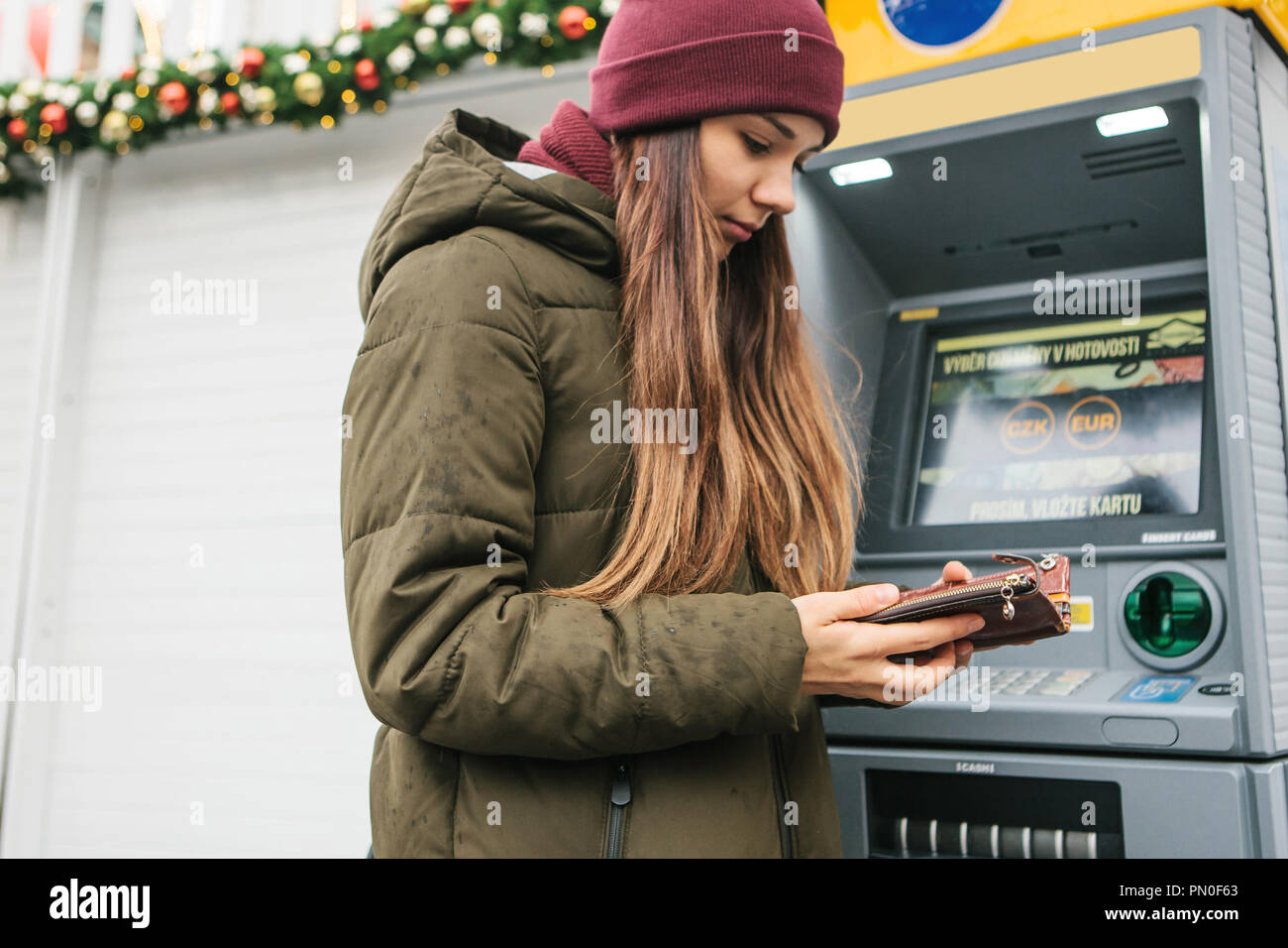 A young woman tourist or girl takes money from an ATM in Prague in the Czech Republic during the Christmas holidays for further tourism around the city. Stock Photo