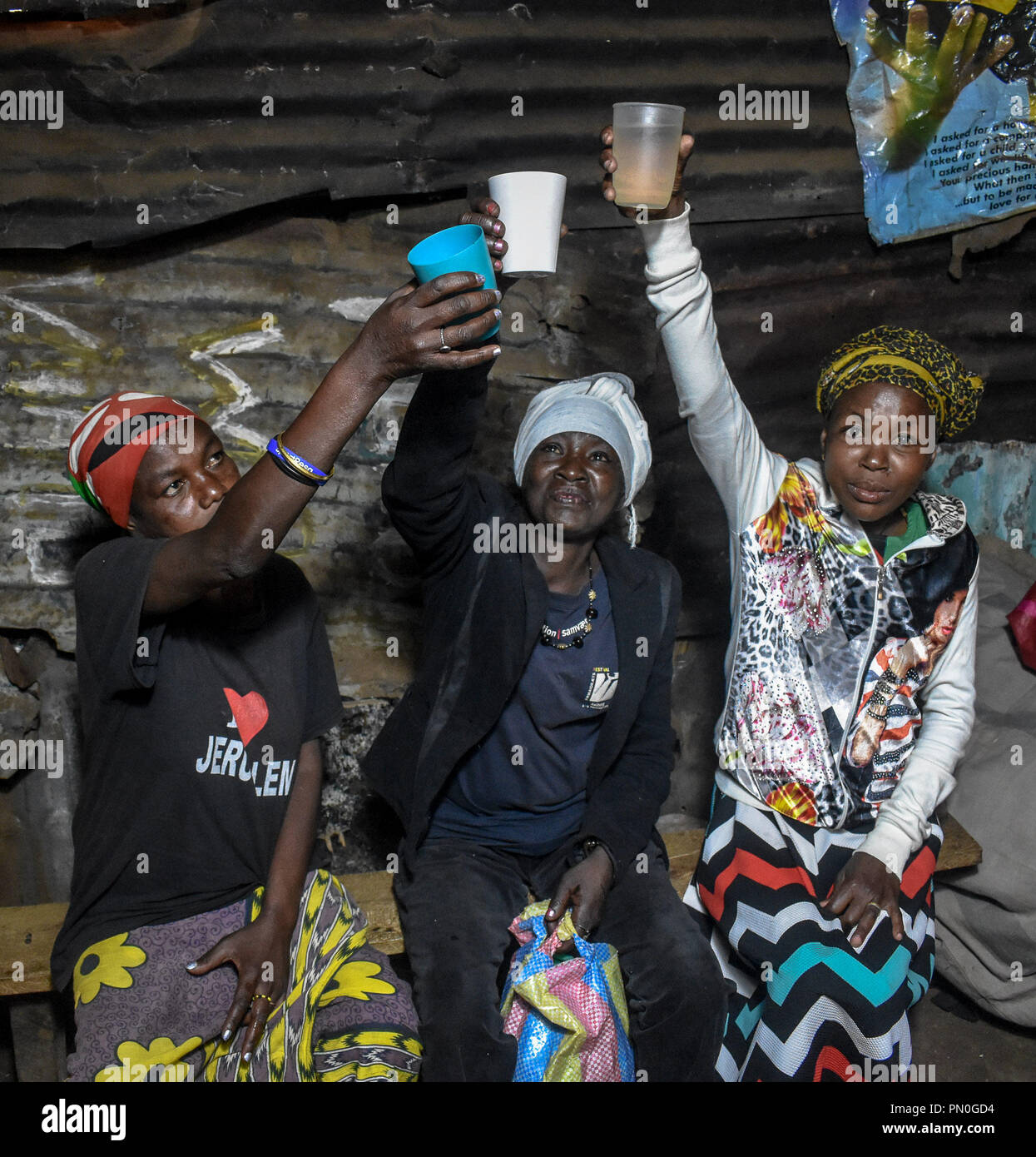 Women seen raising their cups with alcohol. Women from Kibera slums at the age of twenty-five and above are selling alcohol to survive through their daily life. As many women might take alcohol as a way of celebration and as a way of connecting with friends and family during their fun moments, In one of Nairobi largest slum Kibera, women here consume it for different reasons including taking over stress and forgetting about their family problems back home. Stock Photo