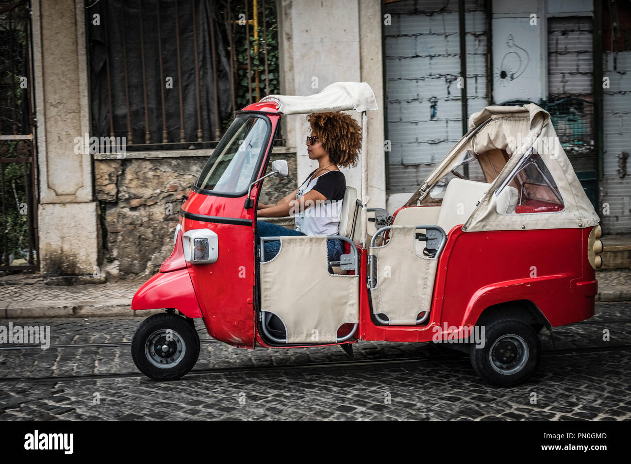 Tourists enjoy a ride in a tuk tuk, three wheeled vehicle in the center of Lisbon, Portugal. Stock Photo