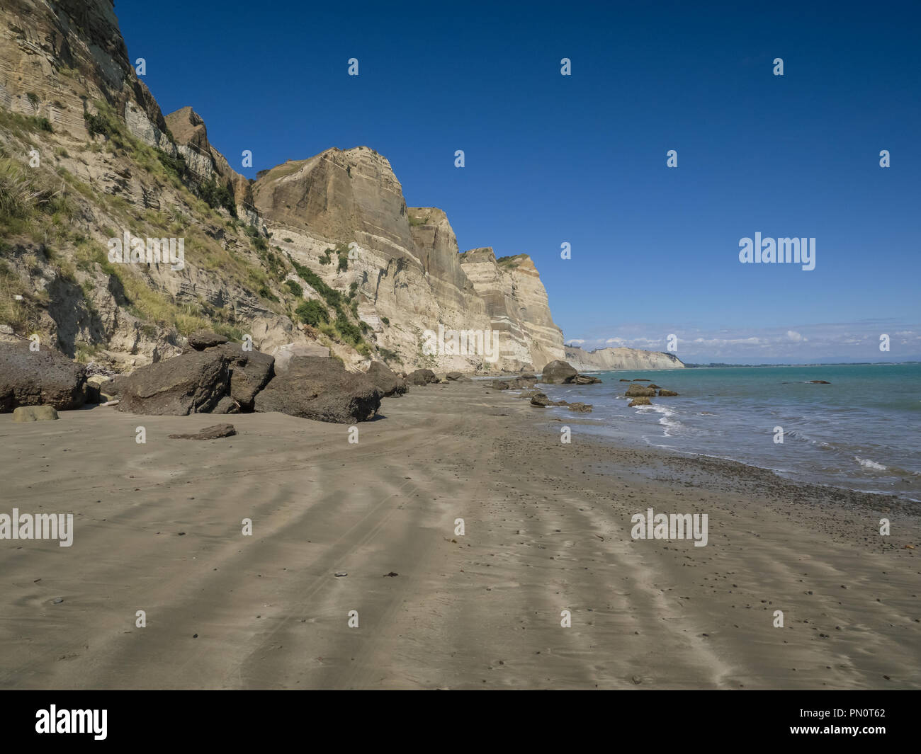 A broad sandy beach below the cliffs on a sunny day at Cape Kidnappers on Hawkes Bay in New Zealand. Stock Photo