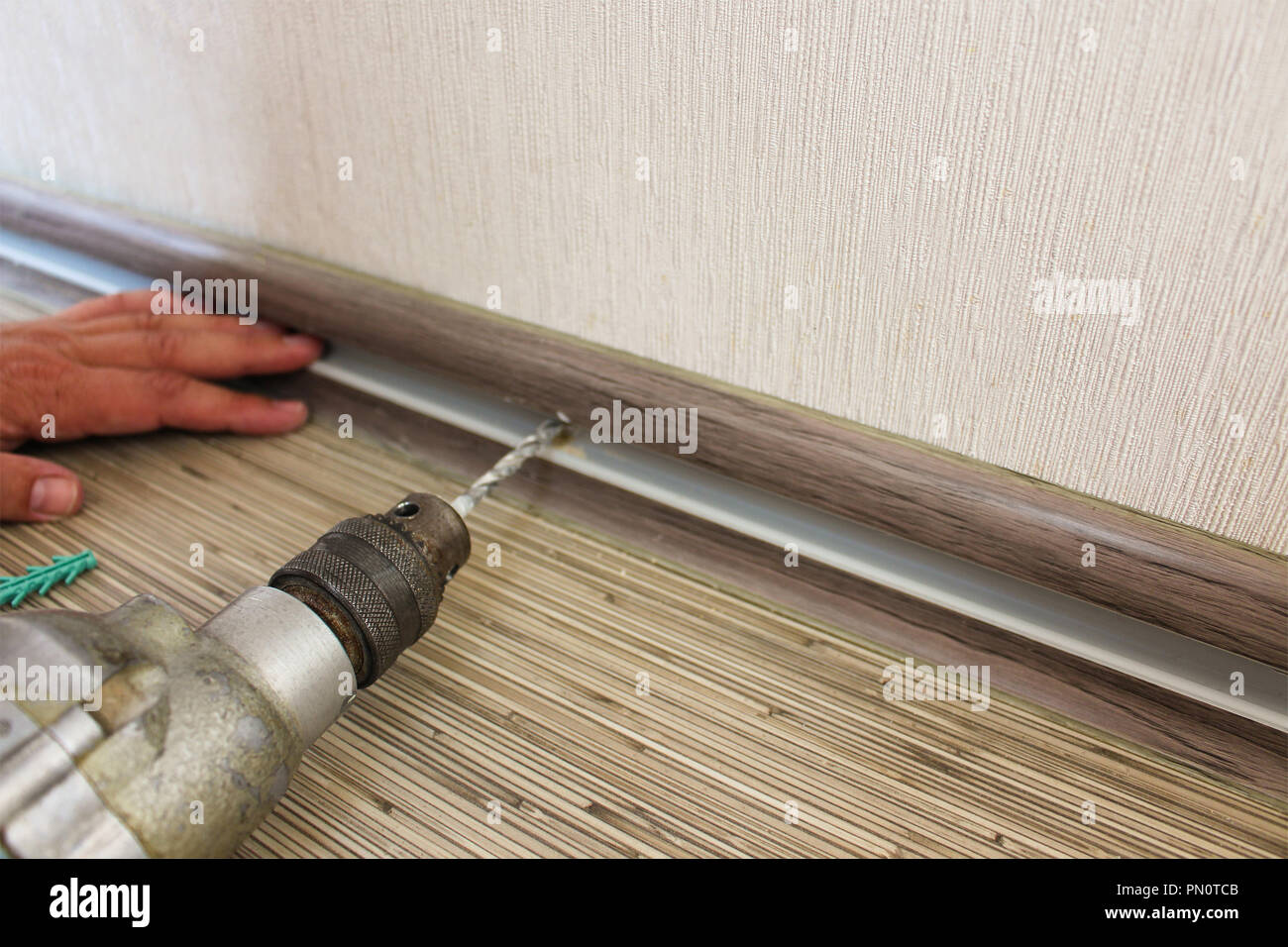 The man secures the baseboard to the wall Stock Photo