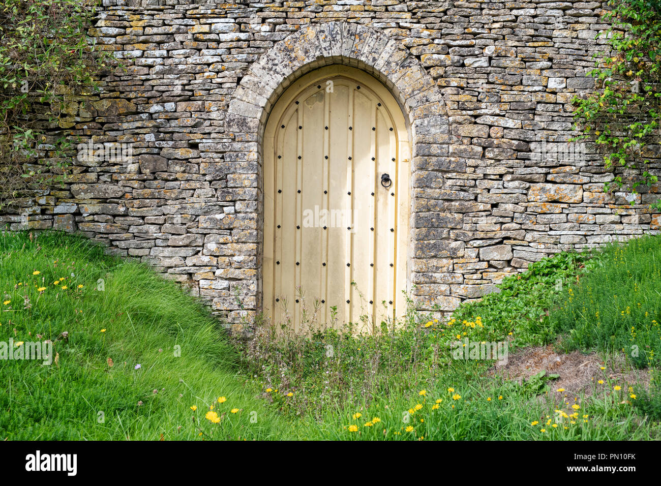 Arched wooden Garden door and cotswold stone wall in front of a house