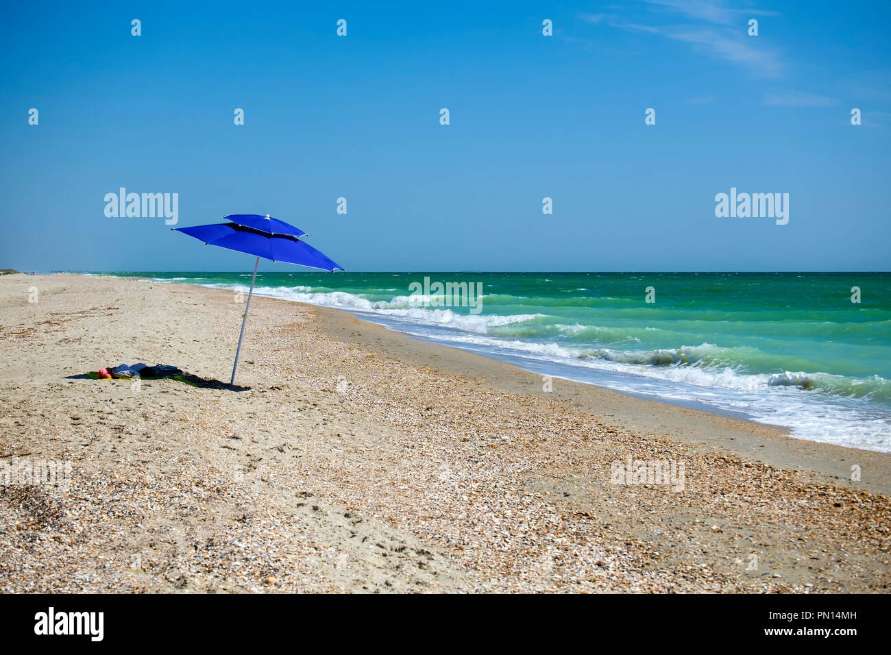 Blue beach umbrella on the shores of the emerald sea (Ukraine, Black Sea, Rasseika) Stock Photo
