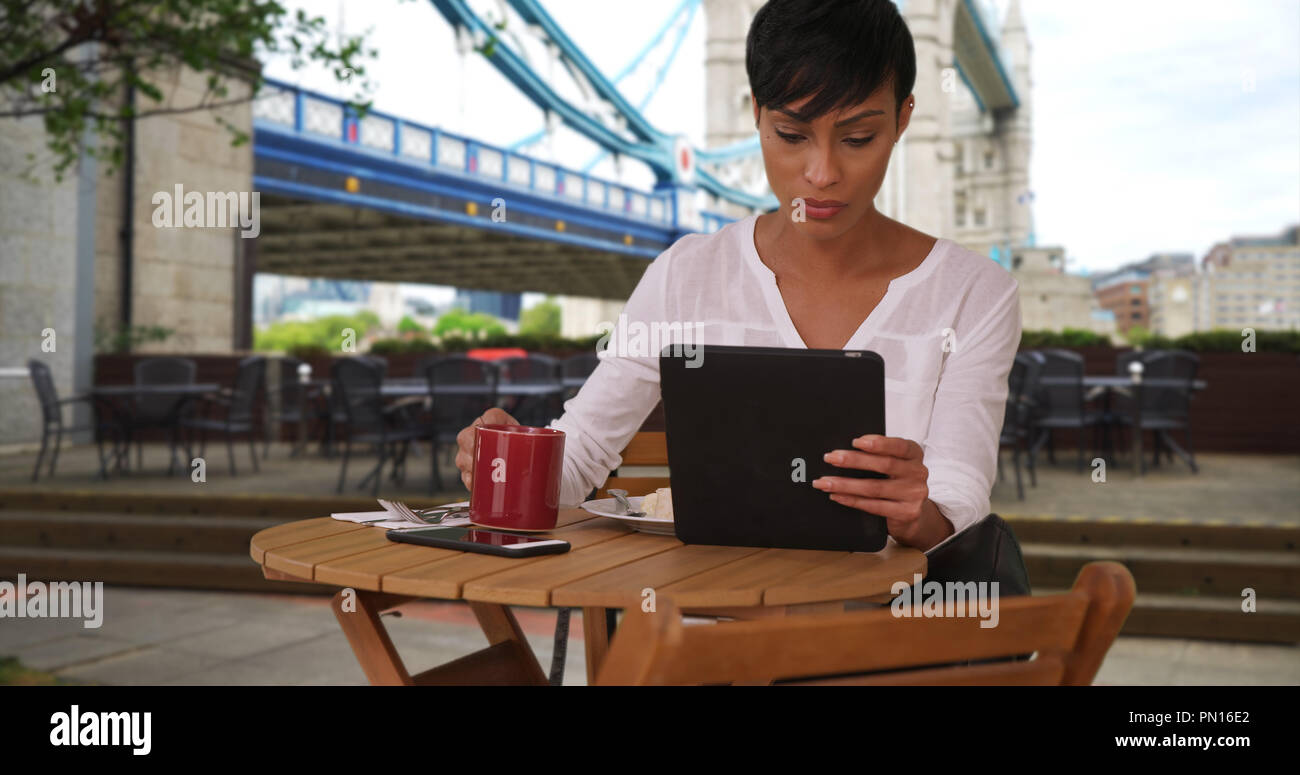 Mixed race female drinking coffee while using tablet near Tower Bridge in London Stock Photo
